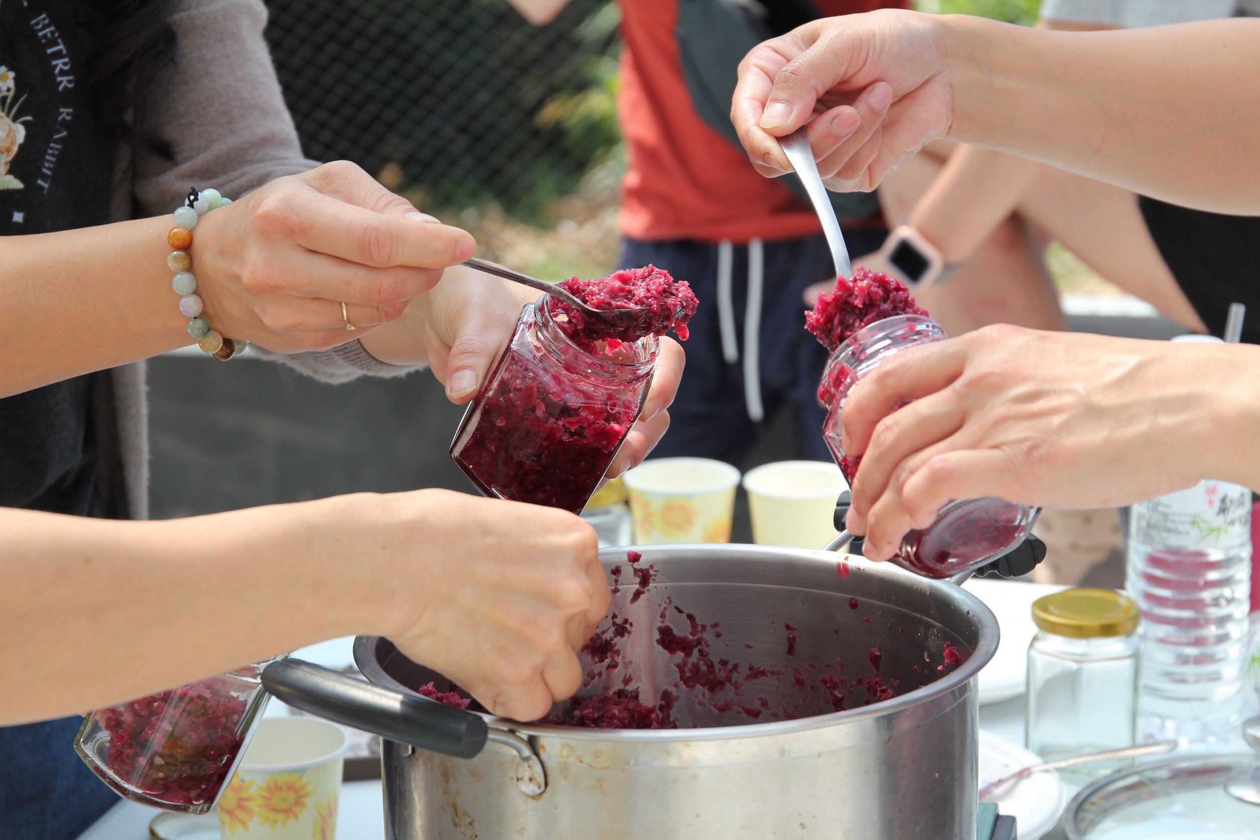 遊客們將煮好的玫瑰花醬一匙匙裝進玻璃罐，專注的動作中帶著成品即將完成的期待。
